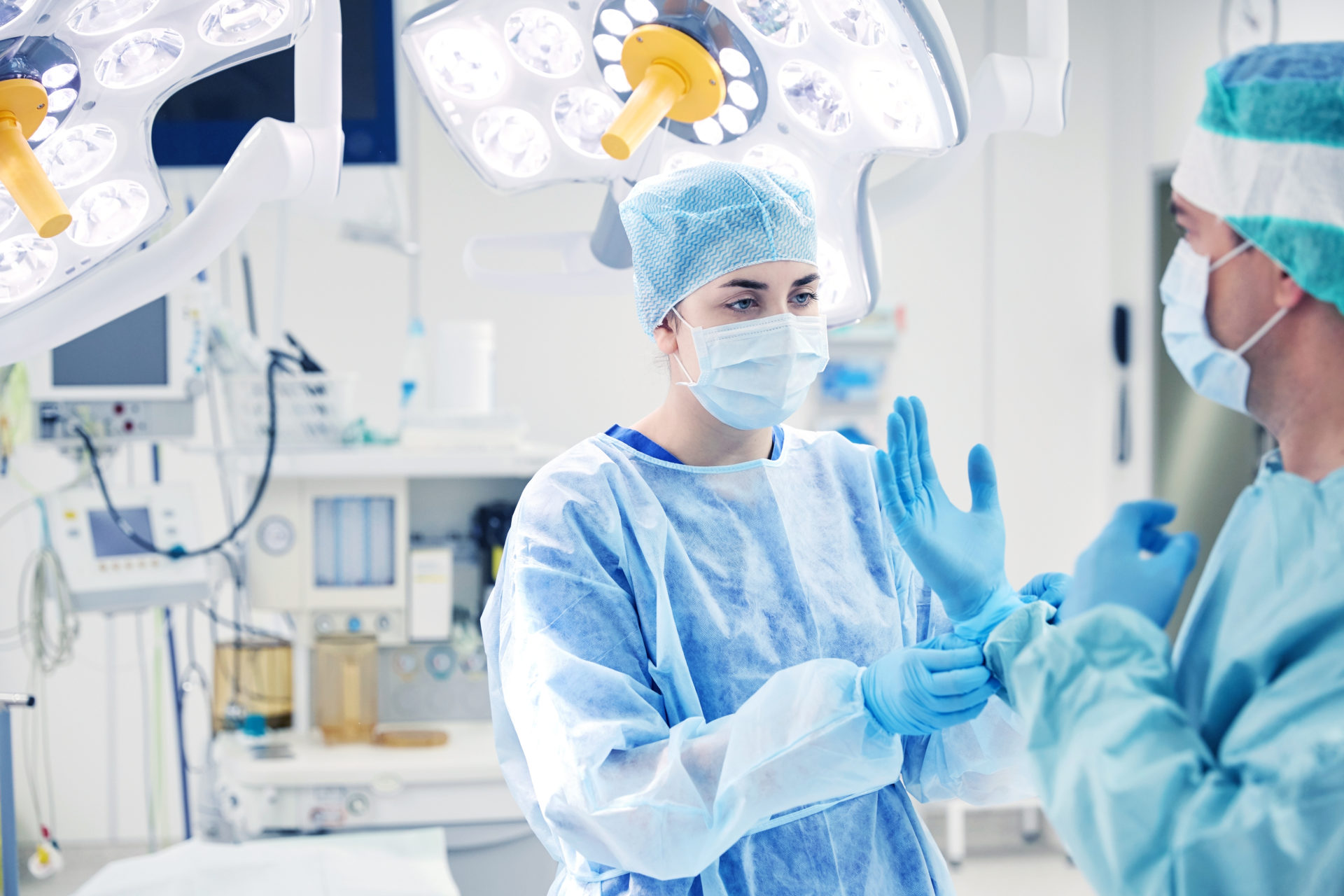 surgery, medicine and people concept - nurse assisting surgeon and helping with gloves in operating room at hospital