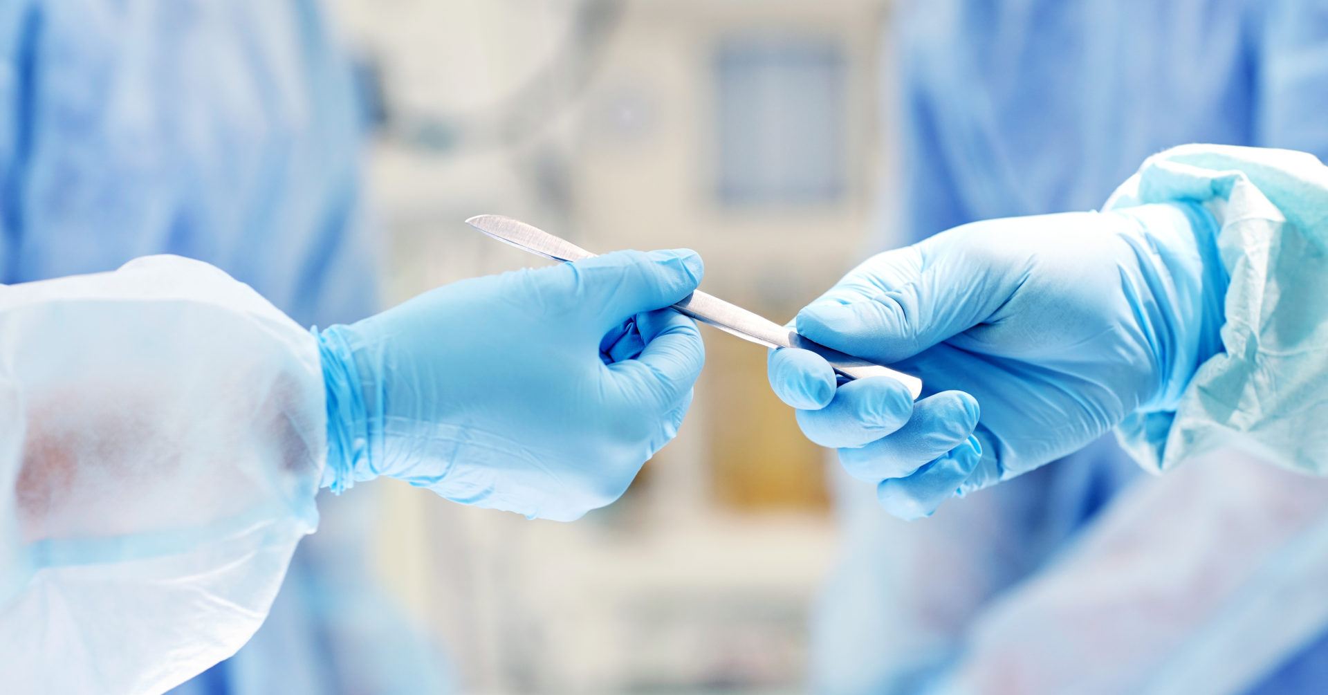 surgery, medicine and people concept - close up of surgeons hands with scalpel at operation in operating room at hospital